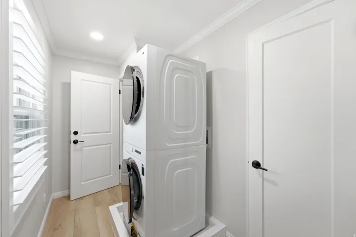 Dedicated laundry area featuring a stacked washer and dryer, wood-finish flooring, plantation shutters, and recessed lighting