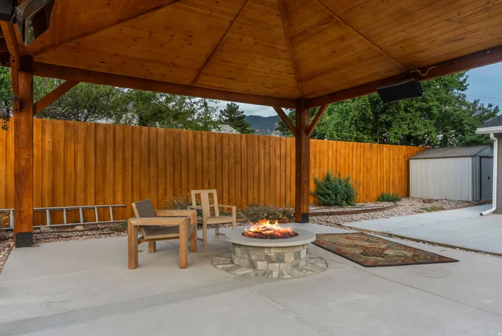 Expansive concrete patio with a wooden gazebo, built-in stone fire pit, and privacy fencing