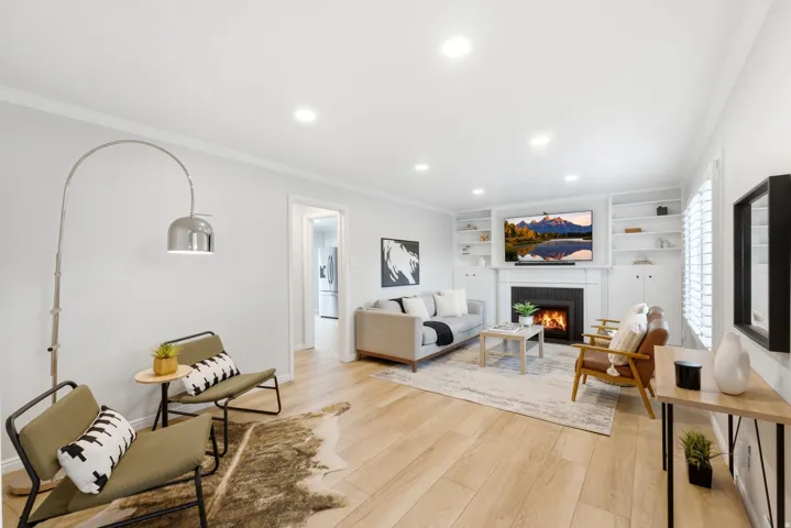 Bright, open-concept living space featuring recessed ceiling lighting, wide-plank wood-finish flooring, and a fireplace with built-in shelving