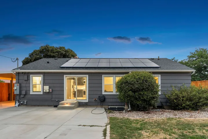 Dark gray siding with white trim, multi-panel solar array, concrete patio, two-step entryway, and sliding glass doors
