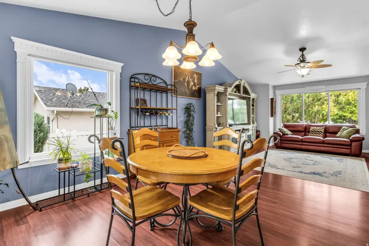 Hardwood-finish flooring, vaulted ceiling, large windows with decorative trim, and a ceiling fan