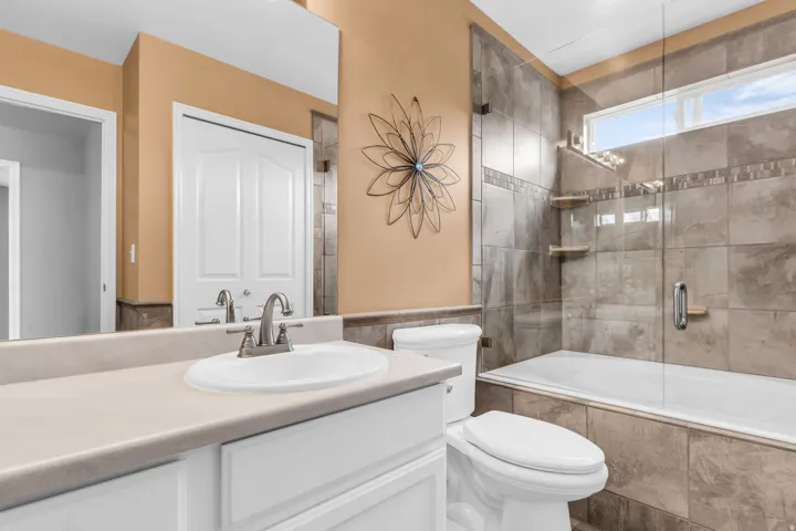 Built-in vanity with single basin sink, brushed nickel faucet, large wall mirror, tiled shower/tub combination with glass enclosure, and transom window