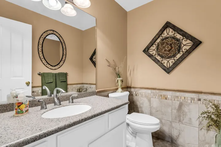 Vanity with a light-toned countertop and an undermount sink, complemented by a large wall mirror and a decorative light fixture
