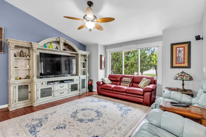 Vaulted ceiling with a ceiling fan, a prominent built-in entertainment center, large windows, and wood-finish flooring