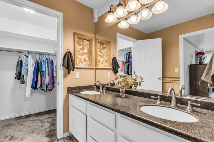 Dual vanity with dark countertop and undermount sinks, wall-mounted light fixture, and white cabinetry