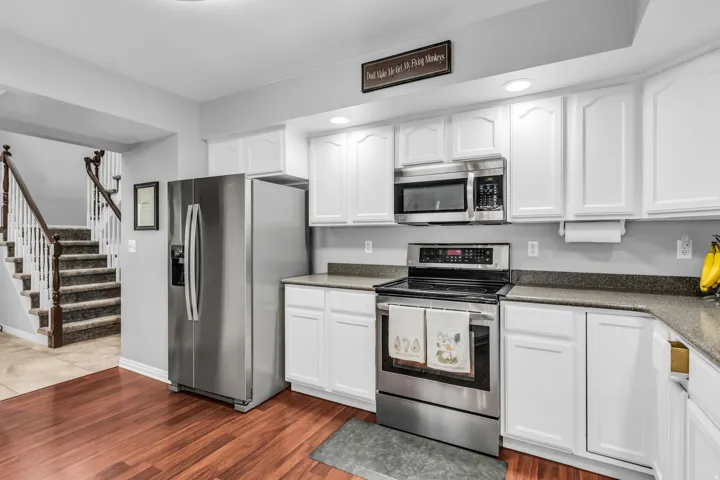 Hardwood-finish flooring, white cabinetry, stainless steel appliances, recessed lighting, and stone-finish countertops