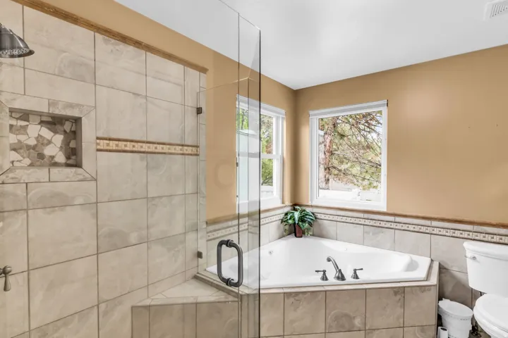 Glass-enclosed shower with a tiled niche and mosaic accent, corner soaking tub, and dual windows