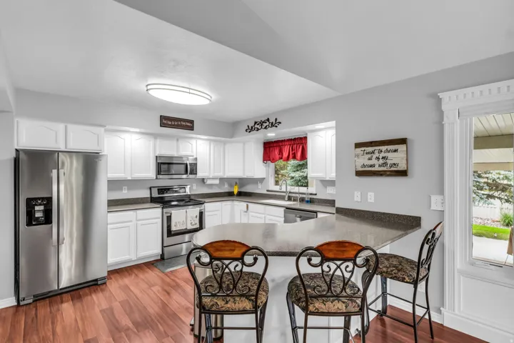 Galley kitchen featuring wood-finish flooring, white cabinetry, stainless steel appliances, and a peninsula with countertop seating