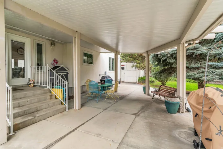 Expansive covered patio featuring a concrete surface, white railings, and mature trees