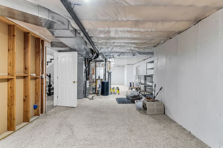 Carpeted floor, exposed ceiling joists, partially finished walls, painted foundation walls, and a white paneled door