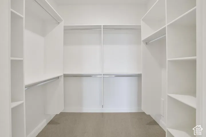 Walk-in closet with built-in shelving, multiple hanging rods, and neutral carpet flooring