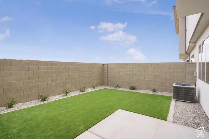 Private backyard featuring artificial turf, concrete patio, gravel borders, and block wall fencing
