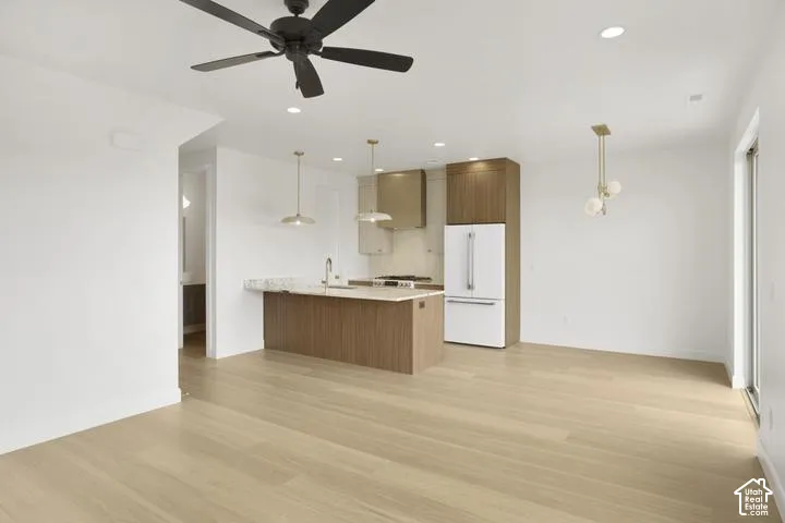 Light wood-finish flooring throughout, kitchen island with stone countertop, stainless steel appliances, recessed ceiling lights, and contemporary ceiling fan
