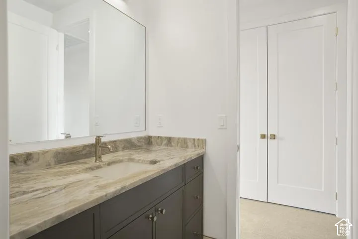 Built-in vanity with an undermount sink, stone countertop, brushed gold-finish faucet, and a large wall-mounted mirror