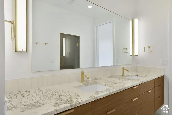 Double vanity with stone countertop, under-mount sinks, wood-finish cabinetry, and gold-finish fixtures