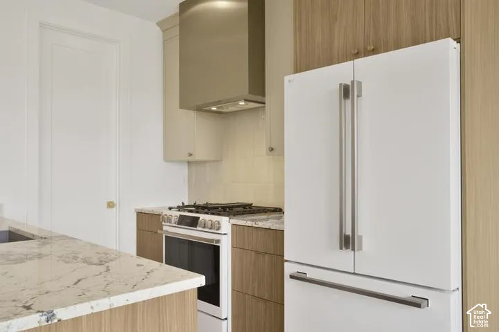 White French door refrigerator, stainless steel range, built-in range hood, wood-finish cabinetry, and light-toned countertops