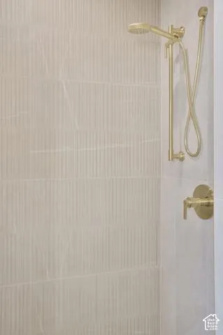 Textured wall tiling with a warm tone, handheld shower fixture, and wall-mounted shower controls