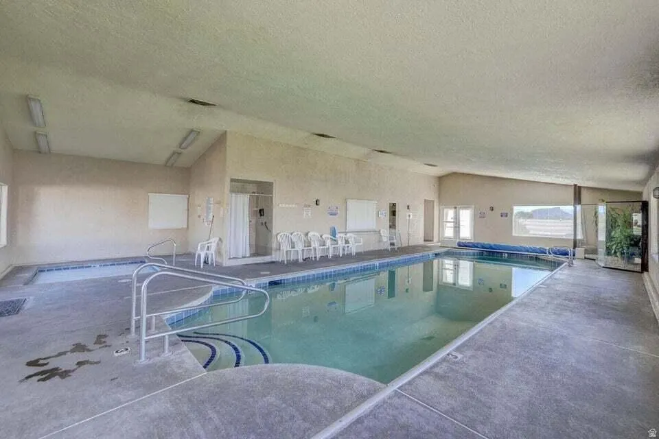 Indoor swimming pool with concrete decking, a built-in spa, and a sloped ceiling