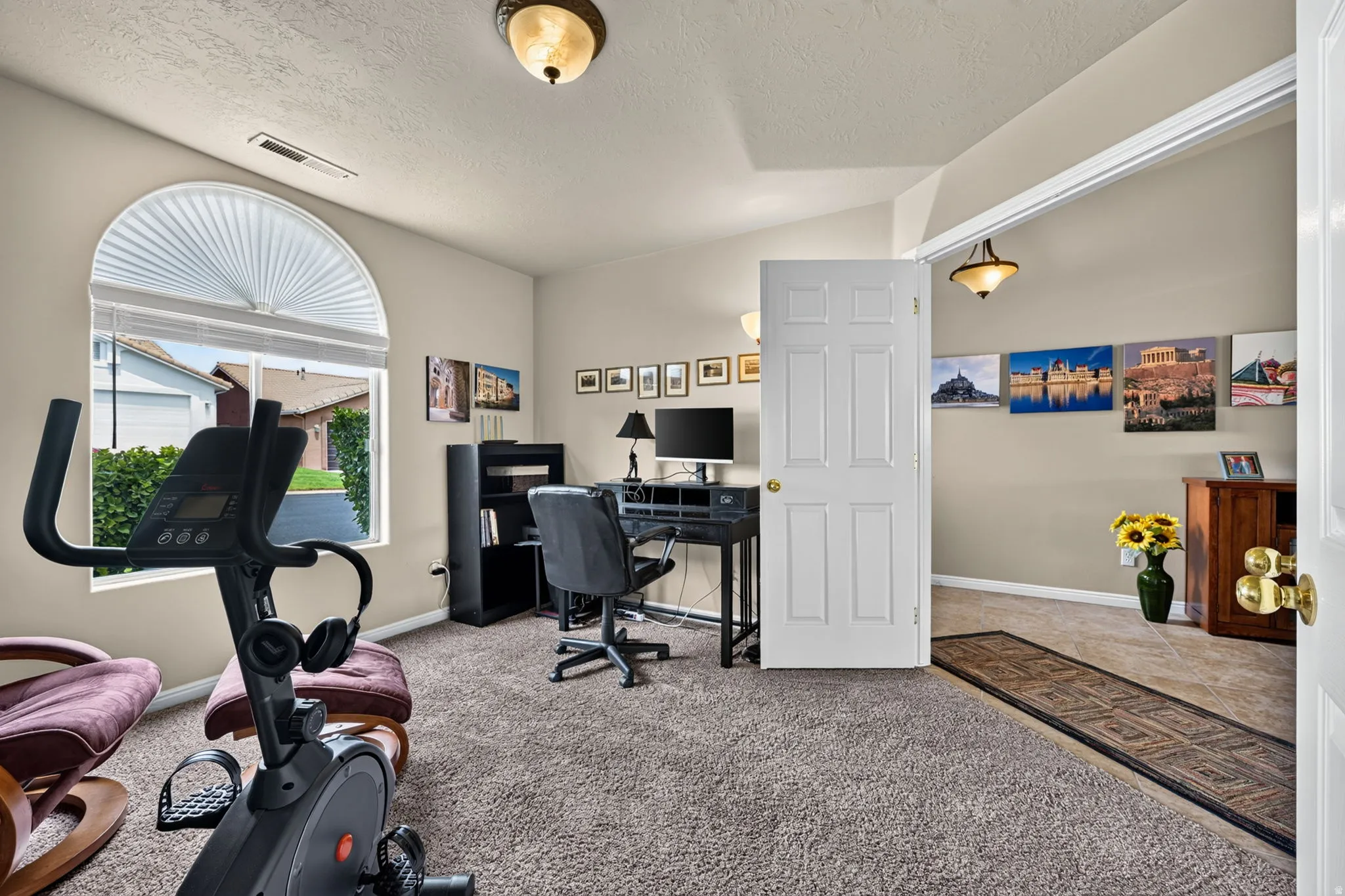 Arched window with pleated shade, neutral wall paint, paneled interior door, ceiling-mounted light fixtures, and carpeted flooring