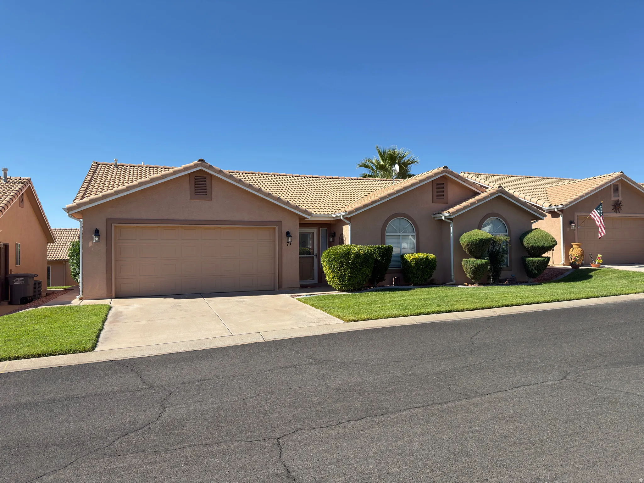 Stucco exterior with a tiled roof, front-facing garage, arched windows, and a landscaped front yard