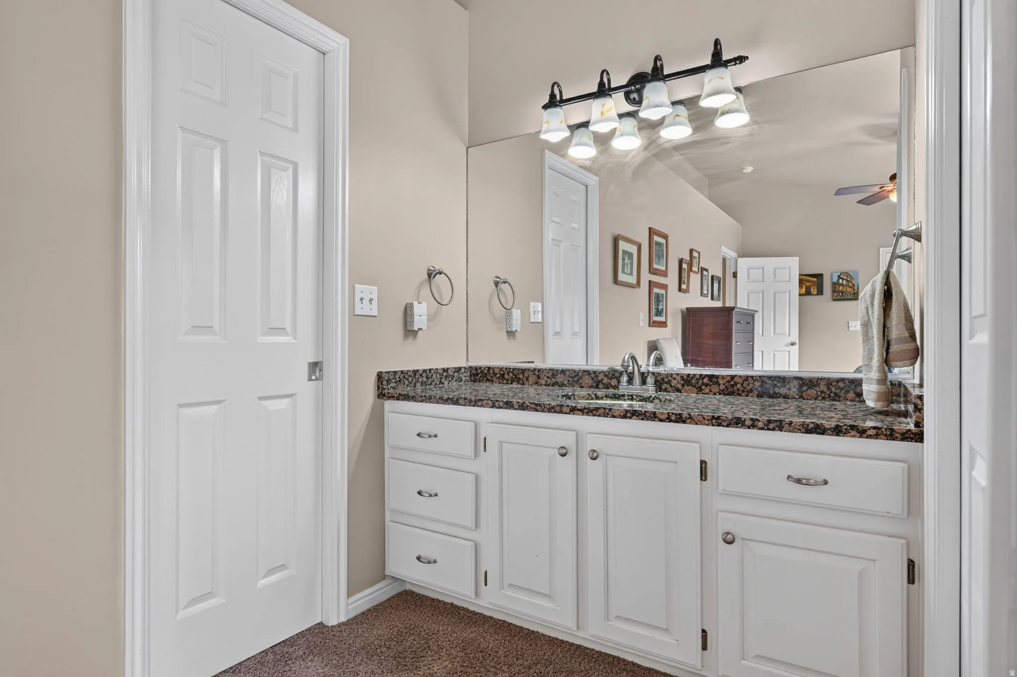 White vanity with polished chrome hardware, a single basin sink, and a dark speckled countertop