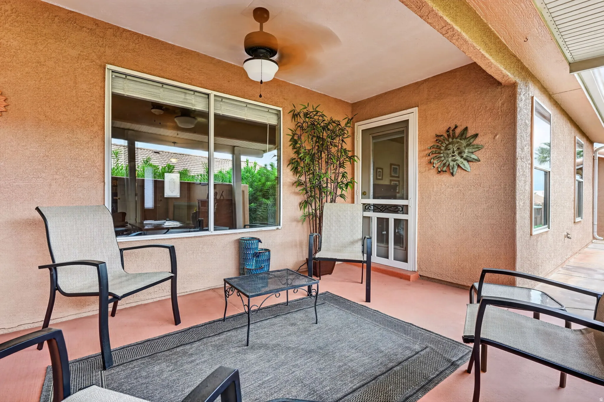 Covered patio featuring a ceiling fan, textured stucco walls, and a screen door