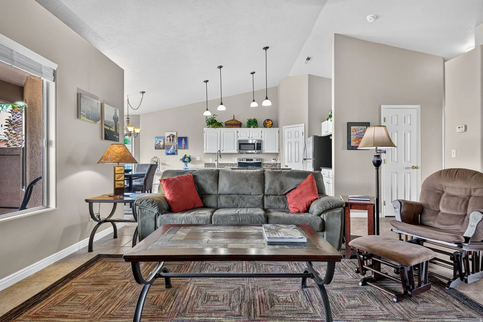 Vaulted ceilings, pendant lighting, white cabinetry, stainless steel appliances, and a window with blinds
