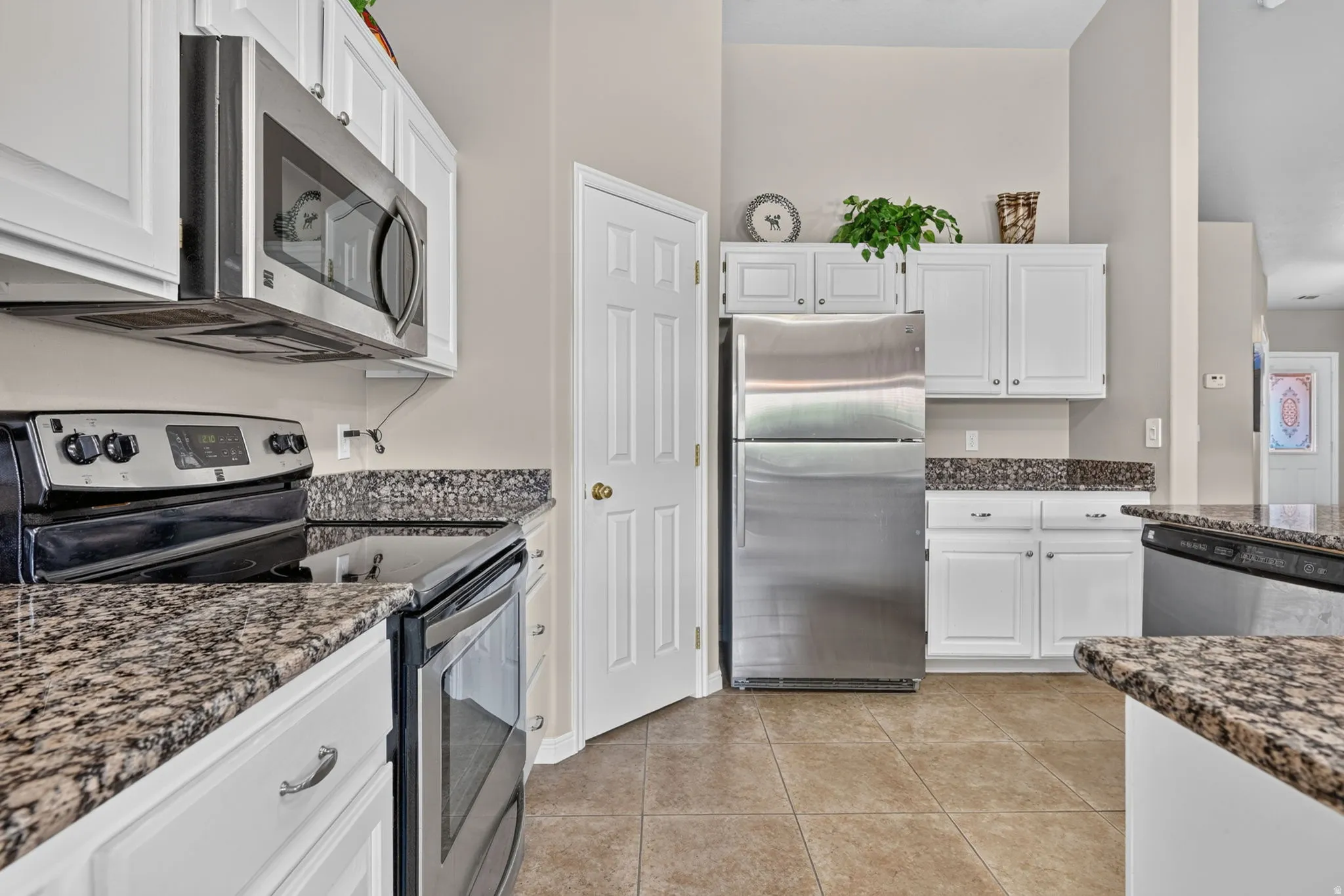 Kitchen featuring white cabinetry, stone-finish countertops, stainless steel appliances, and tile flooring