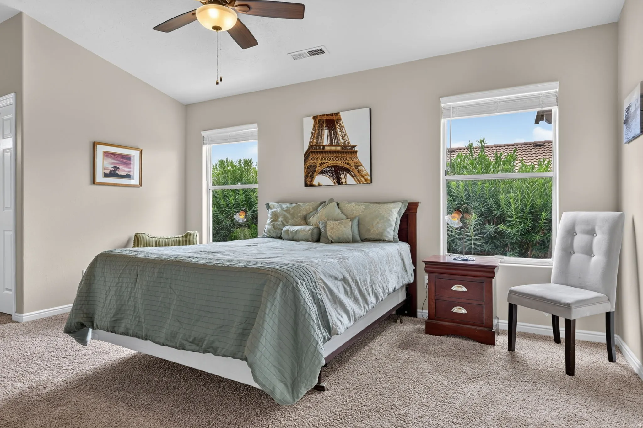 Carpeted bedroom with a ceiling fan light fixture, two windows with blinds, and painted walls