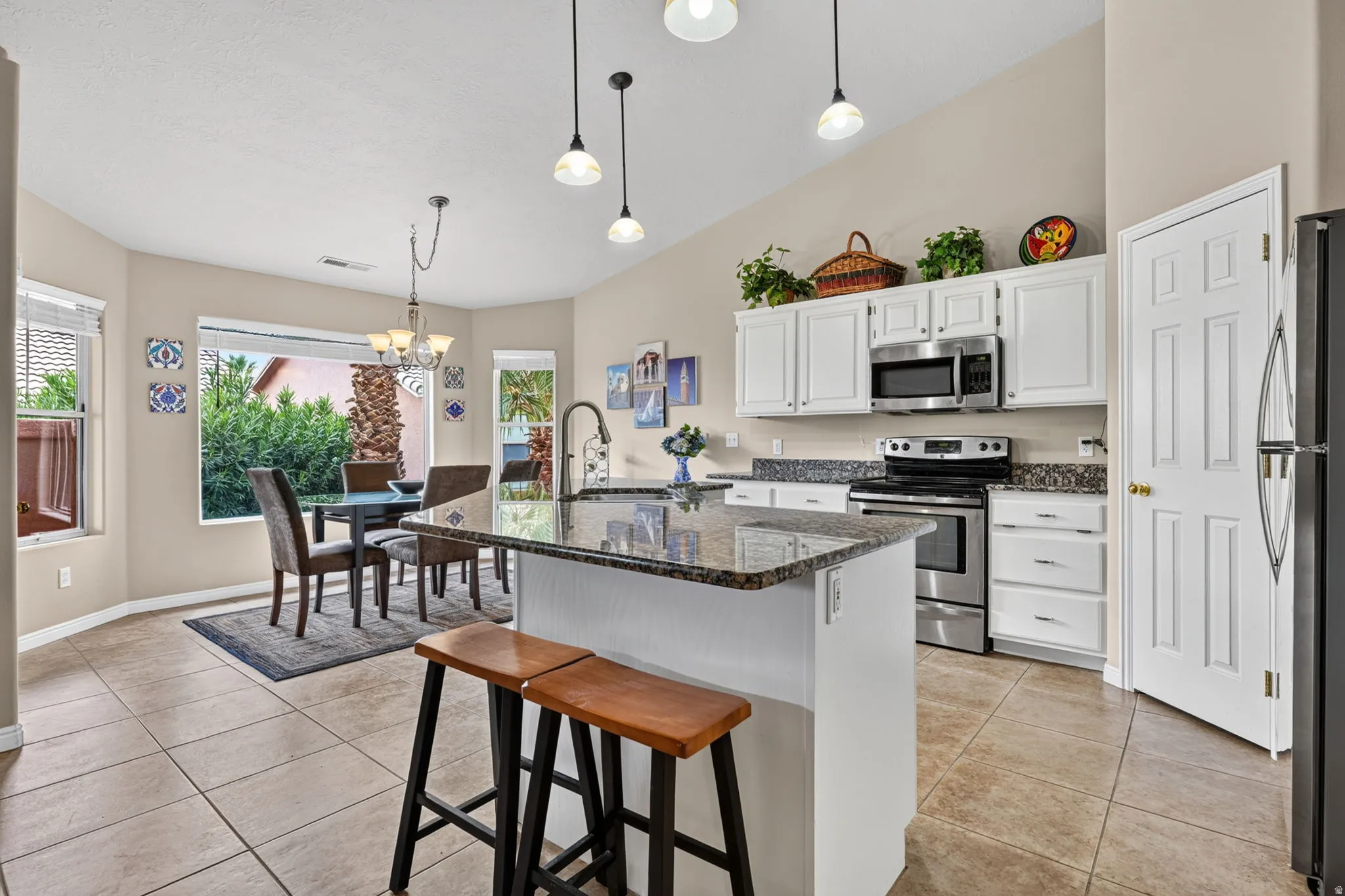 Kitchen featuring a granite-topped island, stainless steel appliances, white cabinetry, and tile flooring