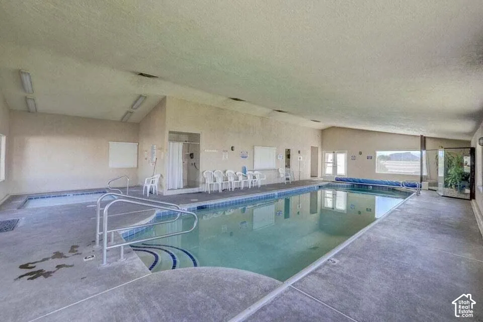Indoor swimming pool with concrete decking, a built-in spa, and a sloped ceiling