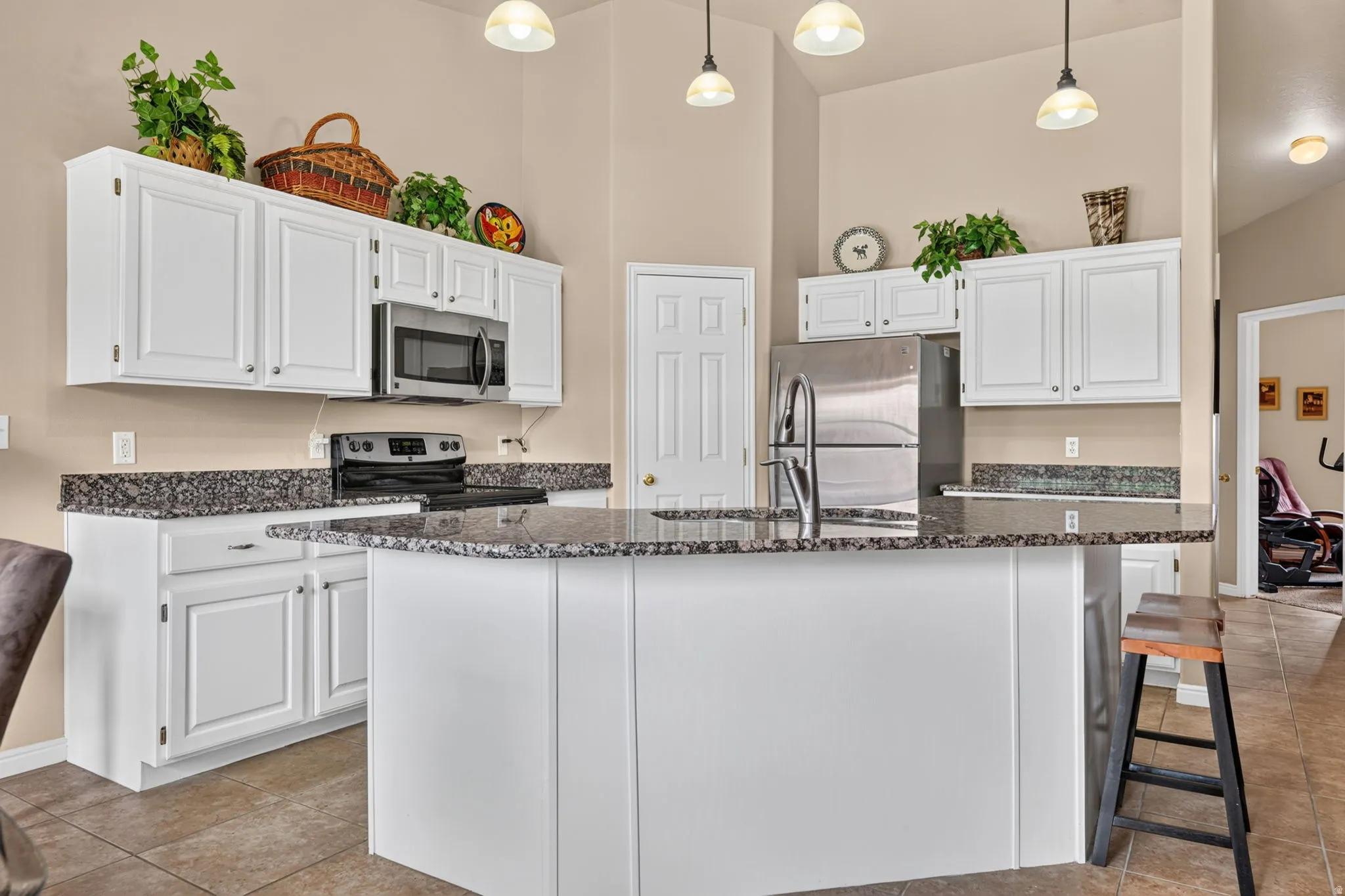 Kitchen featuring white cabinetry, dark speckled countertops, stainless steel appliances, and a central island with a sink
