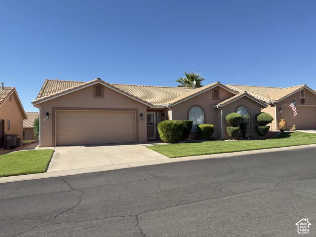 Stucco exterior with a tiled roof, front-facing garage, arched windows, and a landscaped front yard