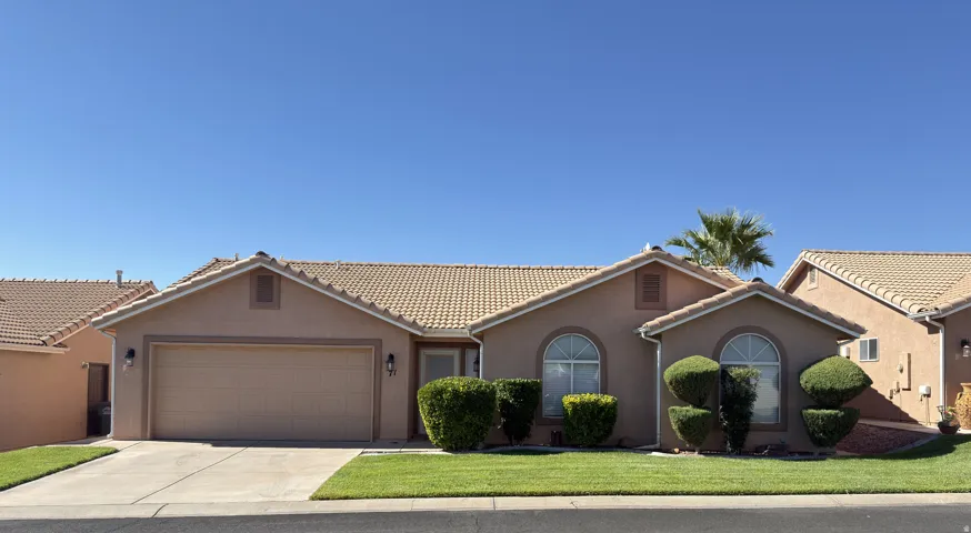 Stucco exterior with a tile roof, an integrated garage, arched windows, and a landscaped front yard with mature shrubbery