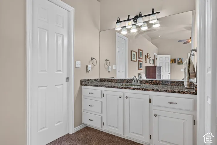 White vanity with polished chrome hardware, a single basin sink, and a dark speckled countertop
