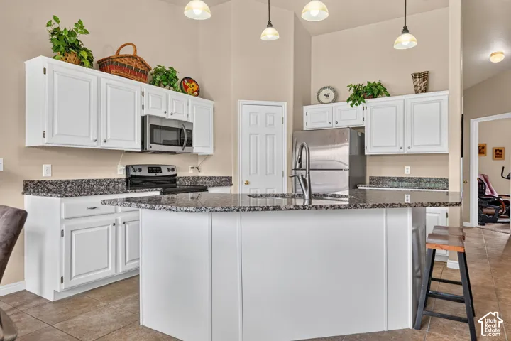 Kitchen featuring white cabinetry, dark speckled countertops, stainless steel appliances, and a central island with a sink