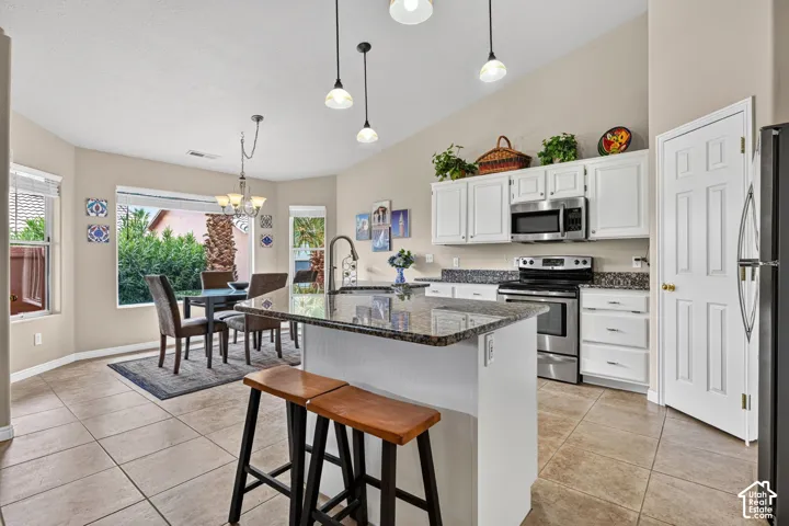 Kitchen featuring a granite-topped island, stainless steel appliances, white cabinetry, and tile flooring