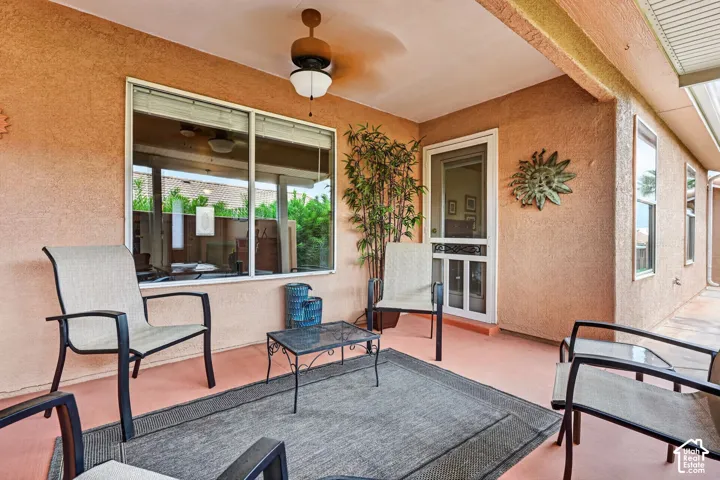 Covered patio featuring a ceiling fan, textured stucco walls, and a screen door