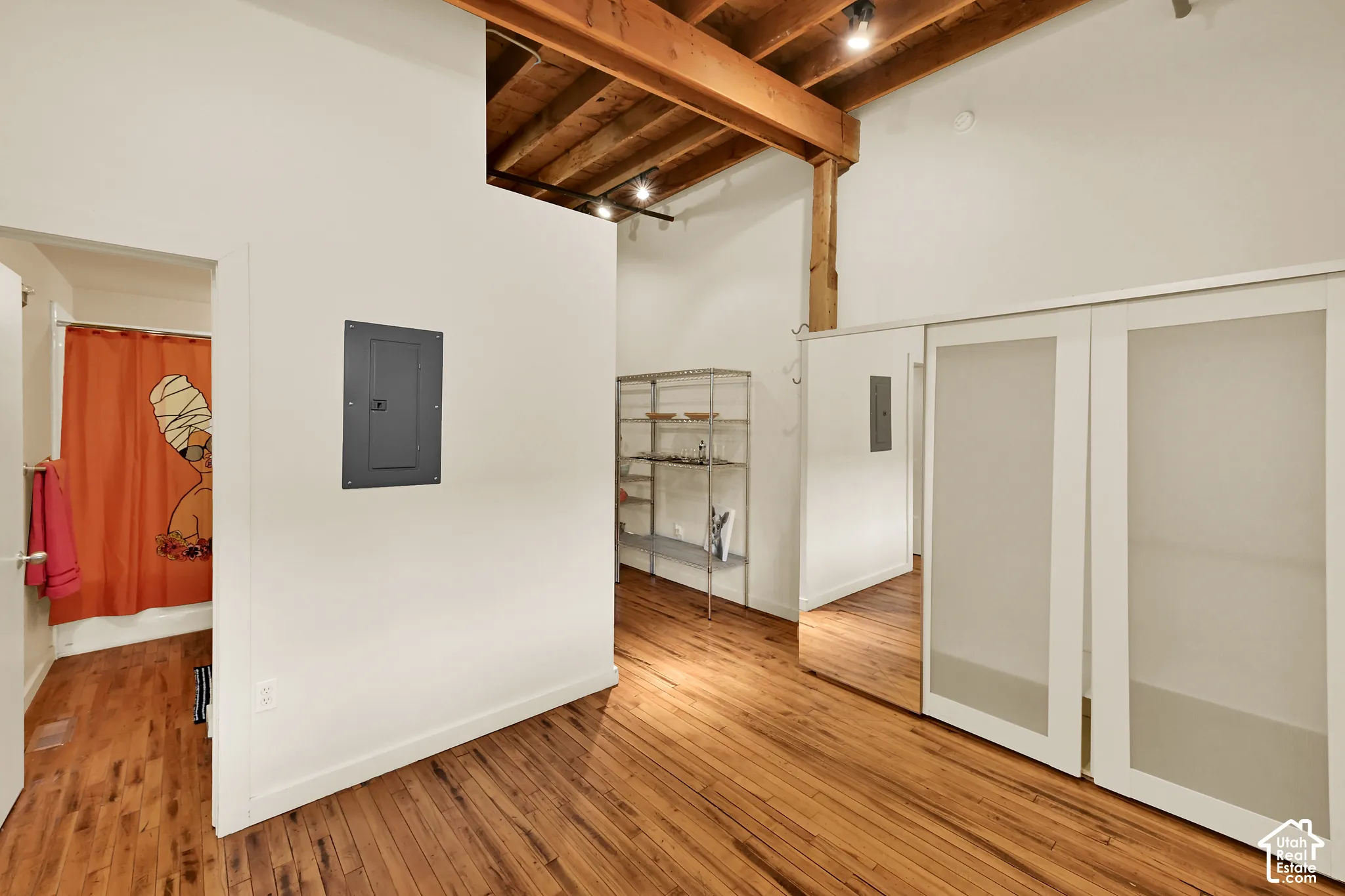 Open loft-style space featuring exposed wooden beam ceiling with recessed lighting, warm wood-finish flooring throughout, and clean white walls