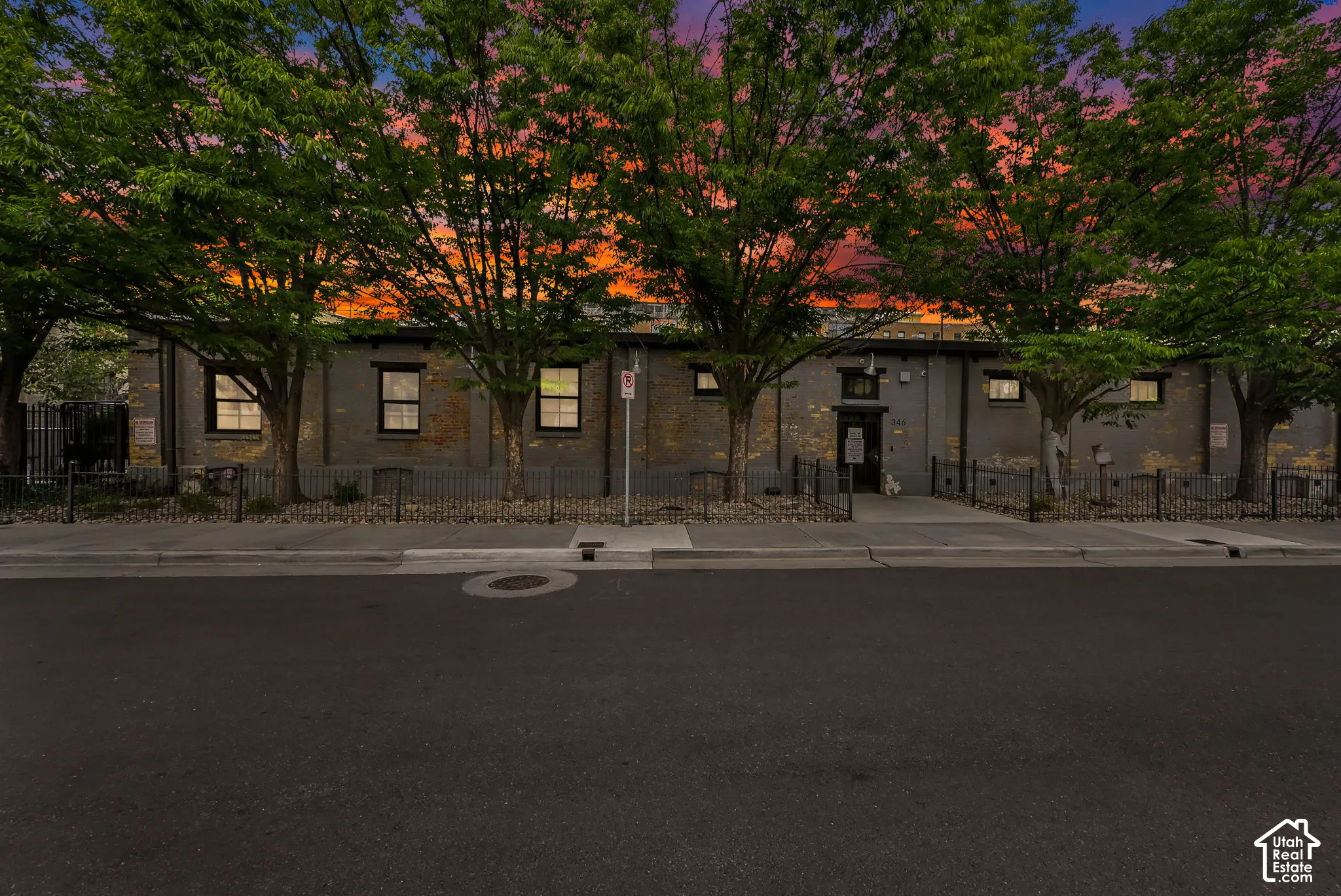 Brick exterior with multiple windows, a central entry door, and perimeter fencing