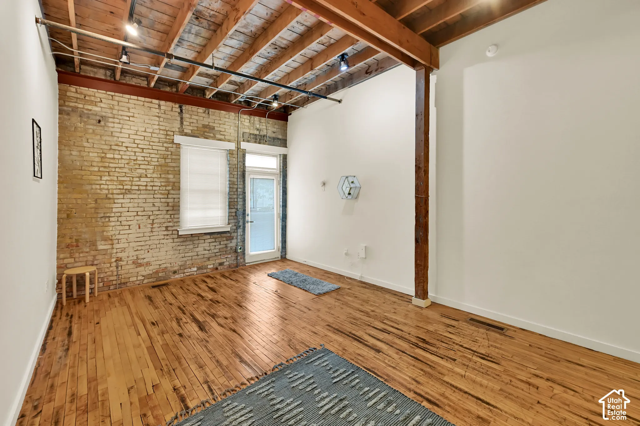 Spacious open floor plan with rich wood-finish flooring throughout, exposed wooden beam ceiling, and brick accent wall