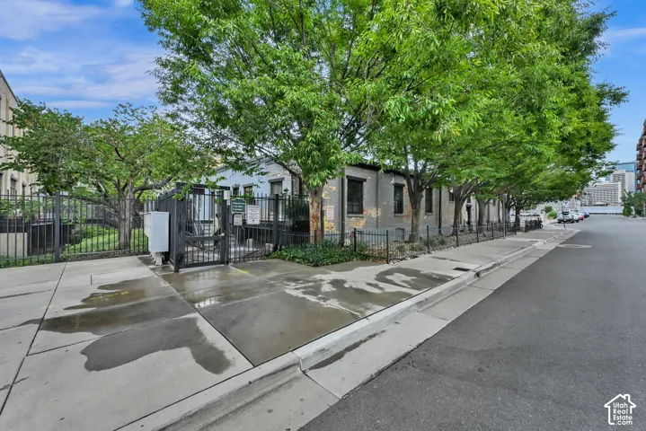 Street-level property featuring a black metal fence, mature trees, and a paved sidewalk