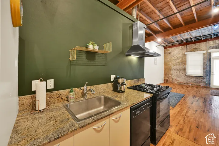 Modern kitchen featuring warm wood cabinetry, countertops, stainless steel sink, and gas range with overhead ventilation