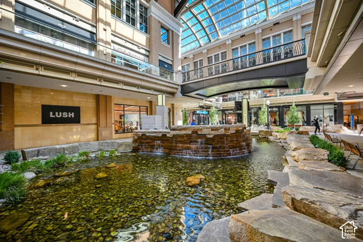 Luxe indoor atrium featuring a serene koi pond with natural stone accents and lush landscaping, anchored by a glass skylight ceiling that floods the space with natural light