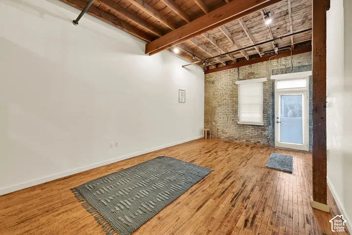 Exposed wood beam ceiling, wood-finish flooring, exposed brick wall, track lighting, and a glass-paneled door