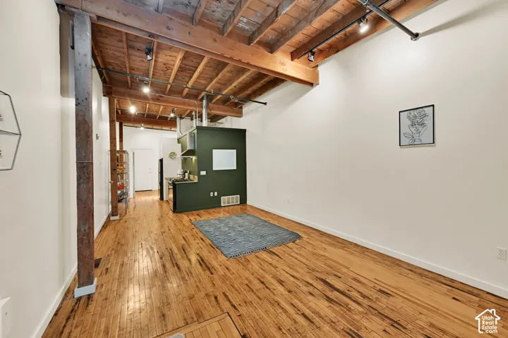 Industrial-modern loft featuring exposed wood beam ceiling with recessed lighting, polished wood-finish flooring throughout, and soaring ceiling heights