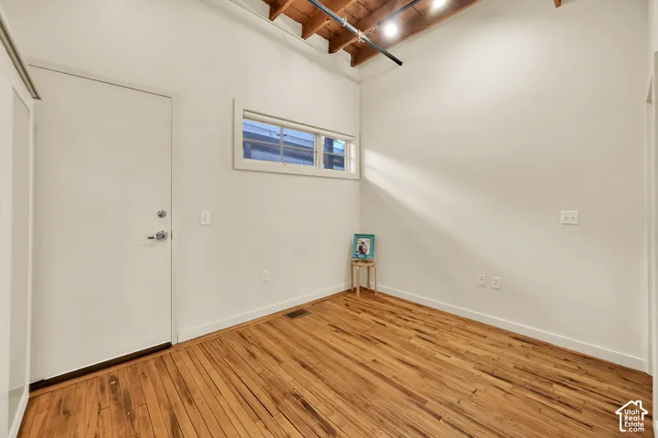 Bright, light-filled room showcasing rich wood-finish flooring, exposed beam ceiling details, and high transom window