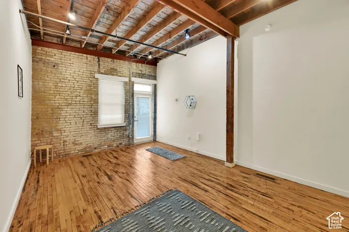 Spacious open floor plan with rich wood-finish flooring throughout, exposed wooden beam ceiling, and brick accent wall