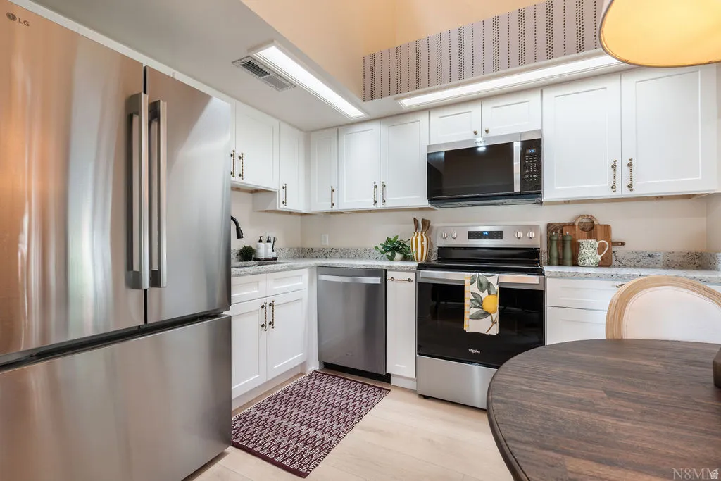Full-height white cabinetry with dark pulls, stainless steel appliances, speckled countertops, and wood-finish flooring