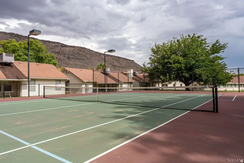 Tennis court with green and red surfacing, perimeter fencing, and overhead lighting